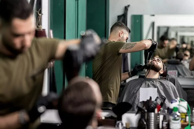 brutal-man-with-a-beard-sits-in-front-of-the-mirror-at-a-barbershop-barber-trims-mens-beard