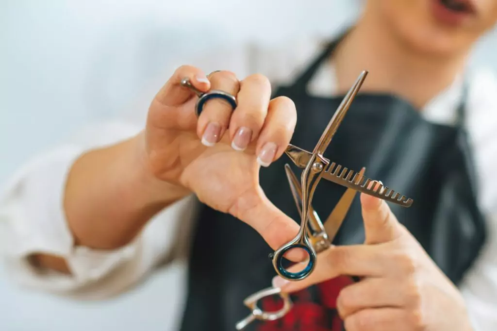 hand-of-a-hairdresser-holding-hairdressing-scissors-explaining-haircutting-techniques-to-students