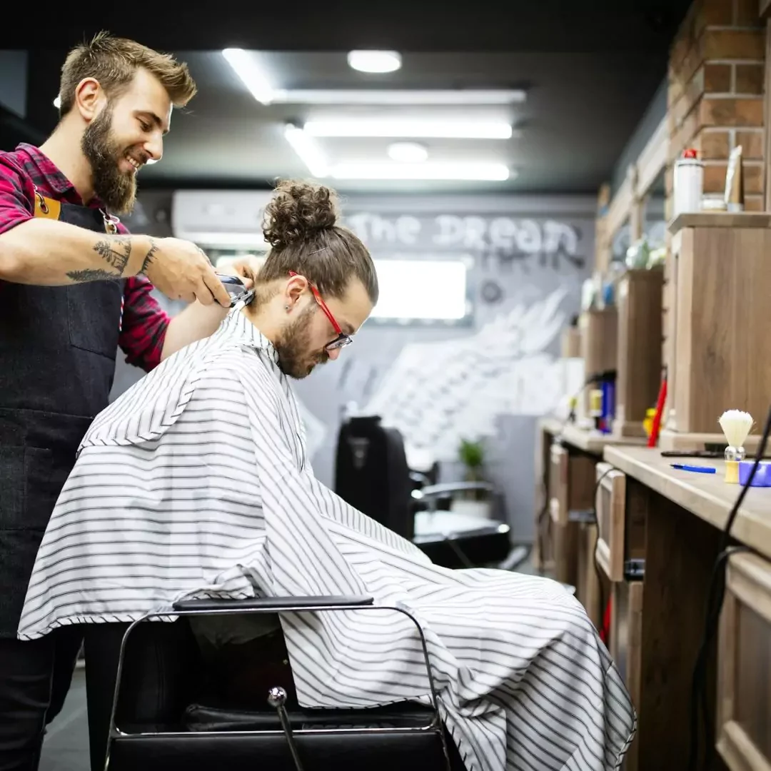 young-bearded-man-getting-haircut-by-hairdresser-while-sitting-in-chair-at-barbershop young-bearded-man-getting-haircut-by-hairdresser-while-sitting-in-chair-at-barbershop
